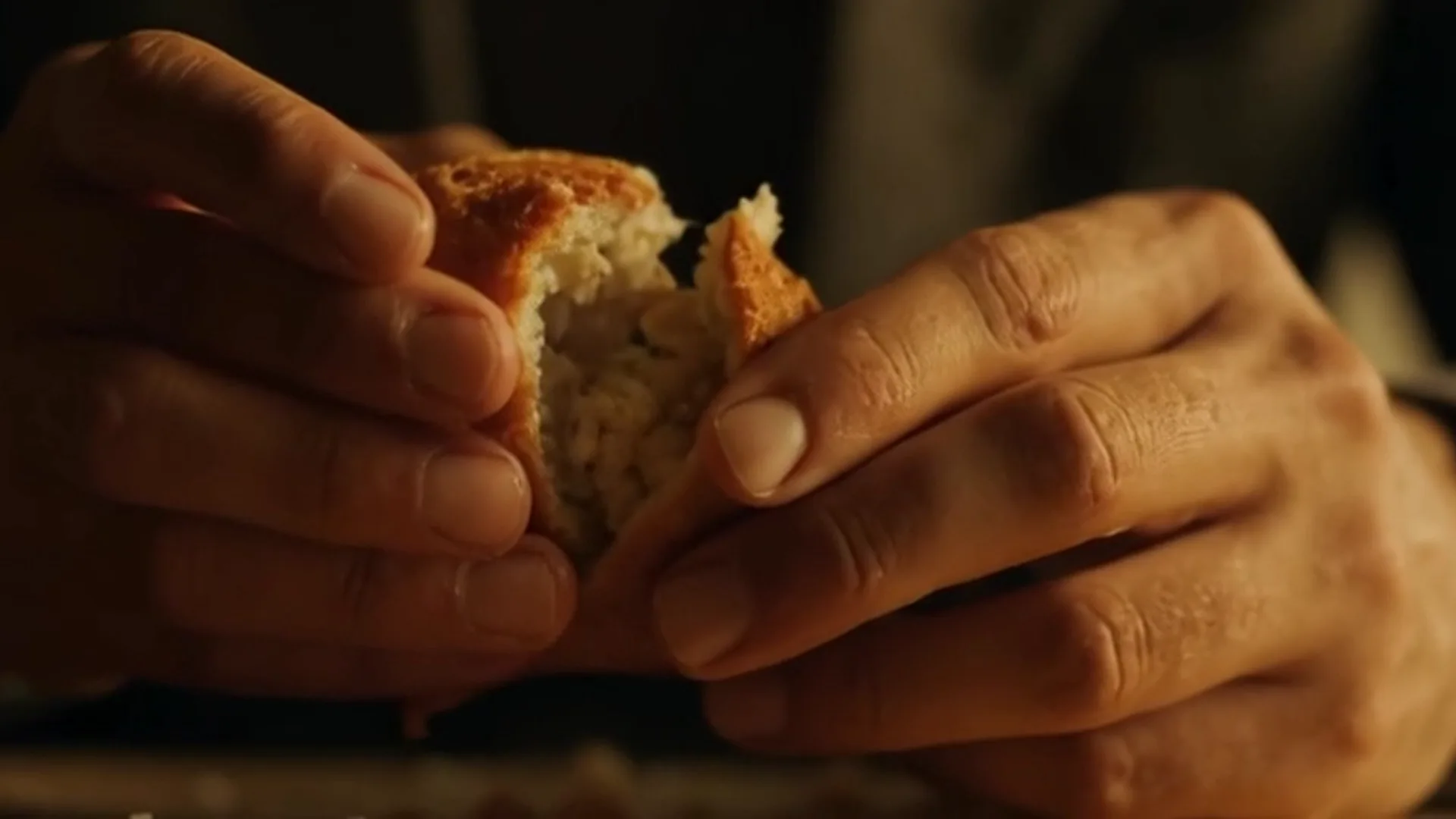 Mãos compartilhando pão, uma passando para a outra, luz quente